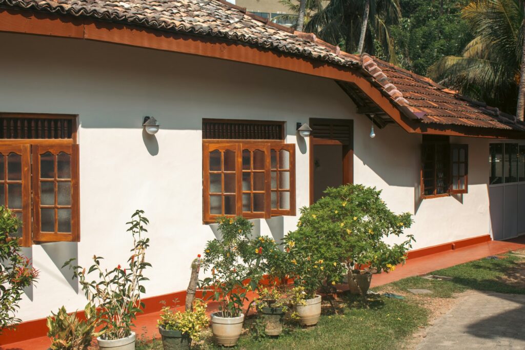 A white guest house with a red tiled roof, wooden windows and a small garden in front