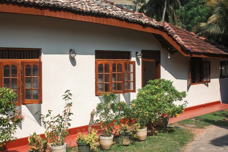 A white Sri Lankan house with a red tiled roof and plants by the door