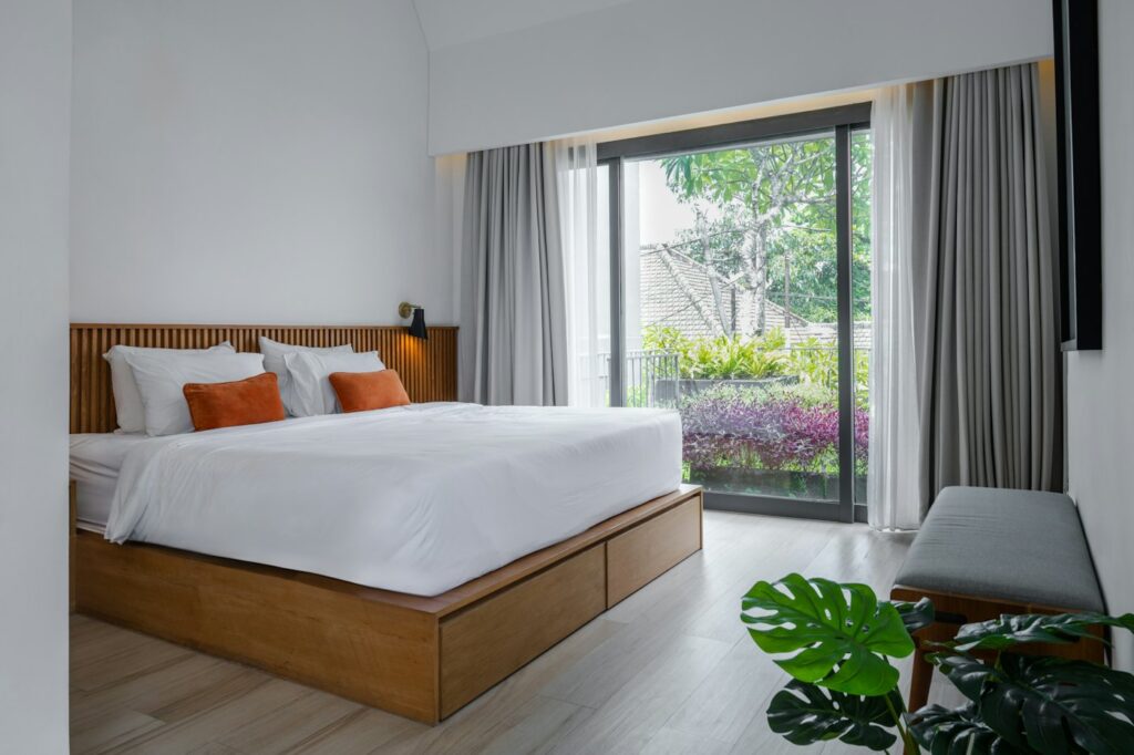 Deluxe Room with a bed facing an open balcony door and green trees outside